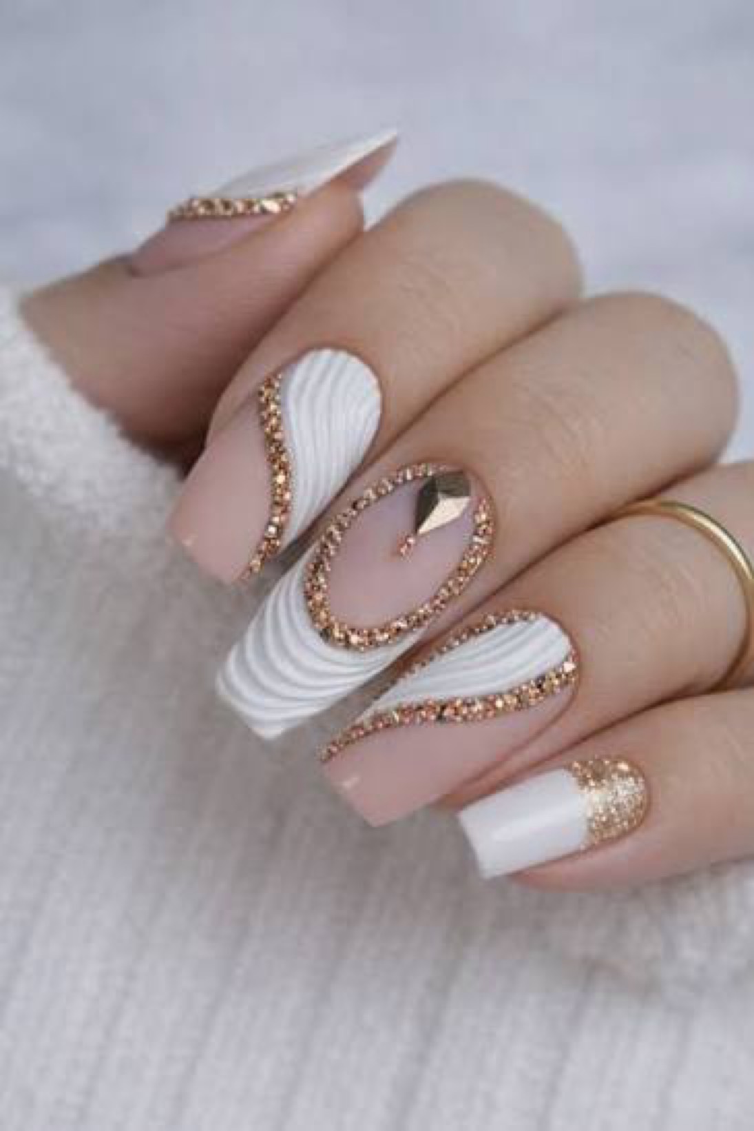 Almond-shaped manicure in nude and milky white with champagne gold rhinestone embellishments